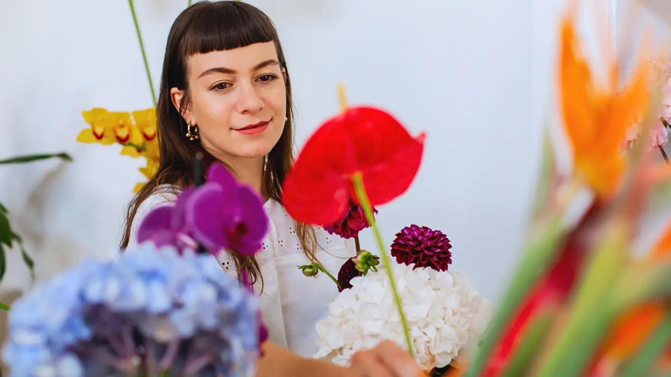 Floristen Anna står och ler omgiven av vackra blommor.