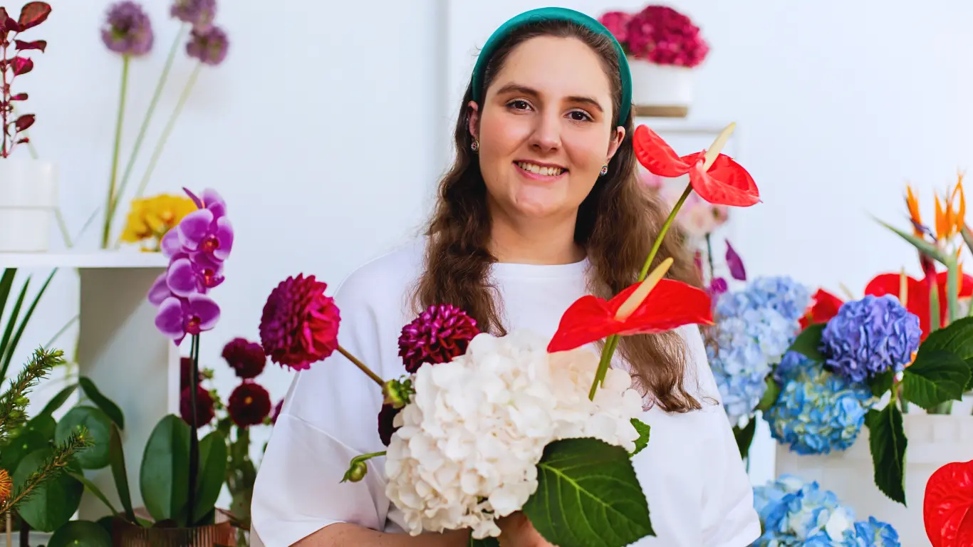 Floristen Sofia ler stort och poserar med blommor i händerna.
